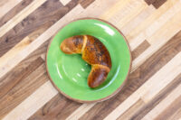 A single golden Loupáčky Czech Poppy Seed Crescent topped with poppy seeds, on a green plate over a wooden table.
