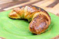 A baked Loupáčky Czech Poppy Seed Crescent, golden and curved, topped with poppy seeds on a green plate.