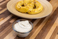 Glass bowl of Mustard Dipping Sauce for Soft Pretzels with herb flecks beside two seeded pretzels