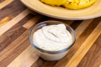 Glass bowl of Mustard Dipping Sauce for Soft Pretzels, speckled and creamy, with pretzels on a wooden plate behind.