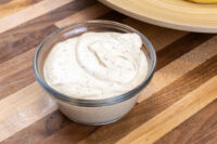 Glass bowl filled with a creamy, speckled Mustard Dipping Sauce sitting on a striped wooden countertop.