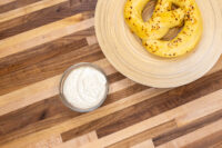 Bowl of Mustard Dipping Sauce for Soft Pretzels beside two seeded pretzels on a striped wood table.