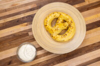 Small bowl of Mustard Dipping Sauce for Soft Pretzels beside two golden pretzels on a wooden table