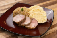 Sliced pork, sauerkraut, and dumpling slices for Pork-Sauerkraut-Dumpling (Vepřo-knedlo-zelo) on a red plate