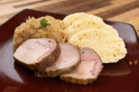 Sliced pork, sauerkraut, and dumpling rounds plated together for Pork-Sauerkraut-Dumpling (Vepřo-knedlo-zelo).