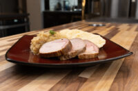 Sliced pork, sauerkraut, and dumpling slices plated for Pork-Sauerkraut-Dumpling (Vepřo-knedlo-zelo) on a dark plate.
