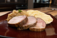Sliced pork with sauerkraut and dumpling rounds arranged on a dark plate for Vepřo-knedlo-zelo