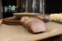 Sliced pork from Pork-Sauerkraut-Dumpling (Vepřo-knedlo-zelo) fanned out on a square plate with a herb garnish.