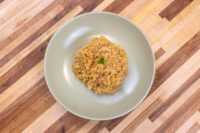 Bowl of golden sautéed Sauerkraut (Kysane Zelí) topped with a small herb garnish on a striped wooden table.