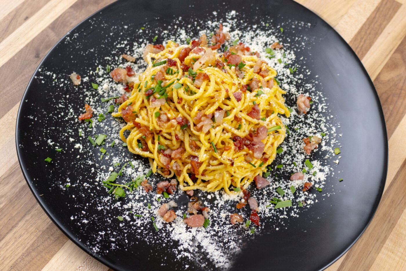 Spaghetti Carbonara with golden egg sauce, crispy bacon bits, herbs, and grated cheese on a black plate