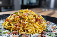 Pile of Spaghetti Carbonara with bacon bits, chives, and parmesan on a black plate