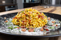 Plated Spaghetti Carbonara with crispy bacon bits, herbs, and grated cheese on a black plate