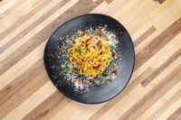 Spaghetti Carbonara twirled on a black plate, topped with bacon bits, herbs, and grated cheese.