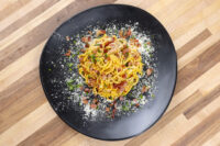 Spaghetti Carbonara twirled on a black plate with creamy orange sauce, bacon bits, herbs, and grated cheese