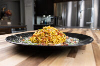 Golden Spaghetti Carbonara twisted high on a black plate with bacon bits and grated cheese