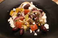 Greek Salad with crumbled feta, kalamata olives, red onion, and tomato on a black plate