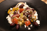 Greek Salad with feta, olives, red onion, tomato, cucumber and peppers on a black plate