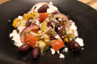 Greek Salad on a black plate with kidney beans, tomato, red onion, olives and crumbled feta.