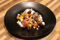Greek Salad with feta, olives, red onion and diced peppers plated on a black dish on a wood table.