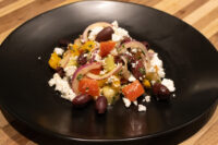 Greek Salad with tomatoes, peppers, red onion, kalamata olives and feta on a black plate.
