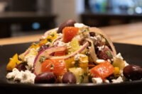 Greek Salad with diced peppers, red onion, olives, and crumbled feta on a dark plate.