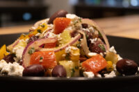 Close-up of Greek Salad with diced peppers, red onion, feta, and olives on a dark plate.