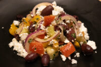 Greek Salad on a black plate with feta, olives, onion, tomato and peppers