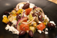 Chopped Greek Salad with feta, kalamata olives, tomato, and red onion on a black plate.