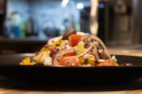 Greek Salad with diced tomatoes, red onion, olives, and feta piled on a dark plate.