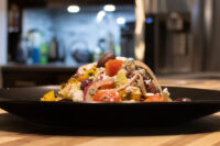 Greek Salad on a black plate with tomatoes, red onion, olives, and feta cheese.