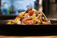 Greek Salad with tomato chunks, red onion, olives and feta piled on a dark plate