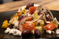 Close-up of Greek Salad with tomato chunks, red onion slices, black olives, and feta on a black plate.
