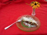 Slice of Apple Strudel dusted with powdered sugar on a green-rimmed glass plate with a fork