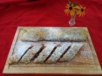 Apple Strudel pastry roll, sliced and dusted with powdered sugar, on a wooden board.