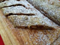 Sliced Apple Strudel on a wooden board, dusted with powdered sugar, filling visible in the cut sections