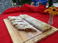 Sliced Apple Strudel on a wooden board, dusted with powdered sugar, showing pale fruit filling.
