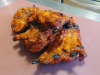 Charred, glazed Czech BBQ – Honey Pork Ribs with red-orange honey sauce on a pink cutting board.