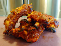 Glazed, charred Czech BBQ – Honey Pork Ribs pieces with a red-orange glaze on a light pink surface.