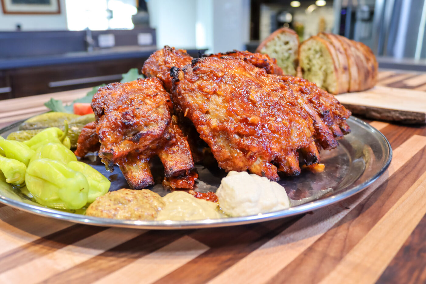 Glazed Czech BBQ – Honey Pork Ribs on a metal plate with pickles, mustard dollops, and bread.