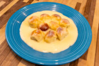 Eight baked buns of Little Buns with Vanilla Pudding (Buchticky s Krémem) sit in pale custard on a teal plate.