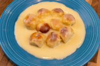 Nine golden-brown Little Buns with Vanilla Pudding (Buchticky s Krémem) arranged in a circle on a blue plate, resting in pale custard sauce.