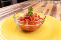 Glass bowl of Czech Tomato Salad with Onion, diced tomatoes and onion, parsley garnish, yellow plate.