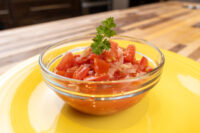 Glass bowl of Czech Tomato Salad with Onion, diced tomato and onion topped with parsley, on a yellow plate.