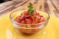 Glass bowl of Czech Tomato Salad with Onion, diced tomatoes and onion topped with parsley, on a yellow plate.