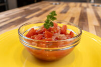 Glass bowl of Czech Tomato Salad with Onion, diced tomato and onion topped with parsley, on a yellow plate.