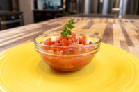 Glass bowl of Czech Tomato Salad with Onion, diced tomato and onion topped with parsley, on a yellow plate