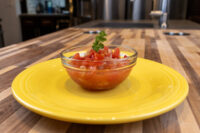 Small glass bowl of diced Czech Tomato Salad topped with parsley, served on a yellow plate.