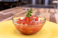 Czech Tomato Salad with Onion in a glass bowl, garnished with parsley, on a yellow plate.