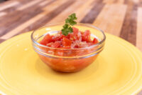 Glass bowl of diced tomato and onion Czech Tomato Salad with Onion, topped with cilantro, on a yellow plate