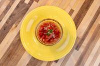 Glass bowl of Czech Tomato Salad with Onion, diced tomatoes and herb garnish, on a yellow plate.